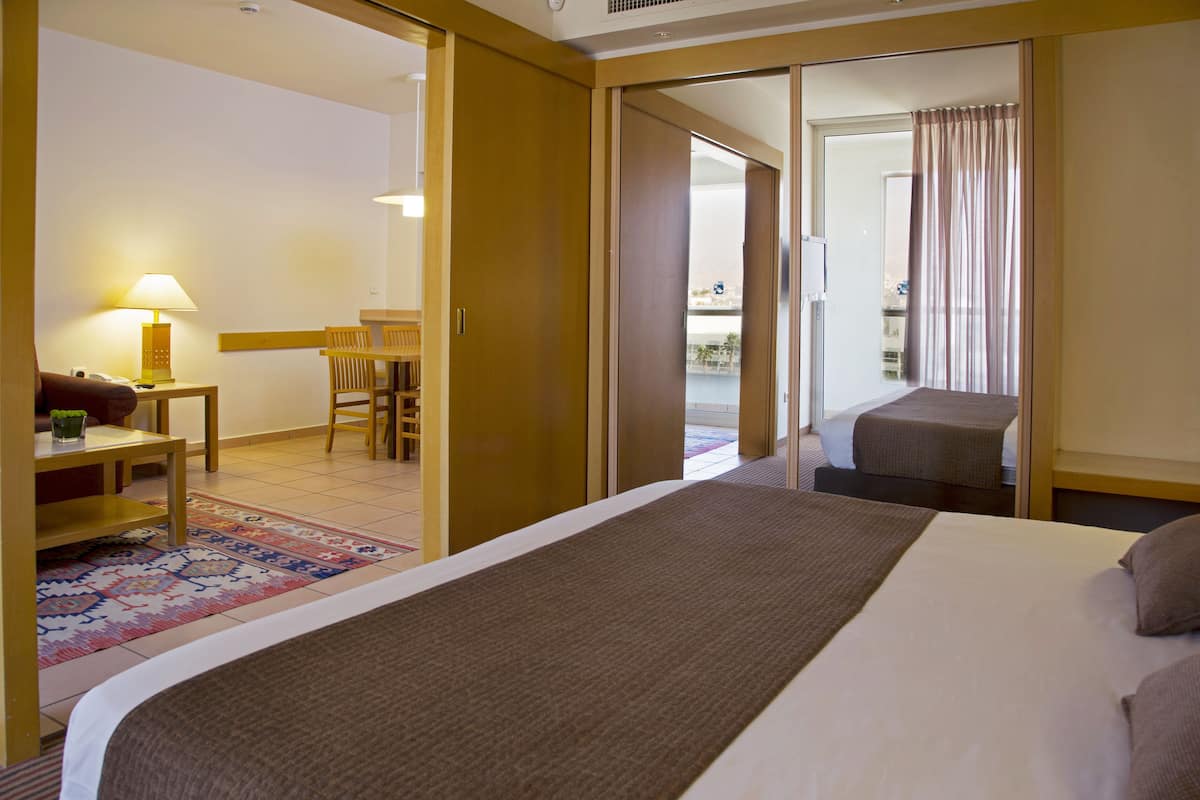 A hotel room with a large bed, a desk with a lamp, a chair, and a view of the balcony.