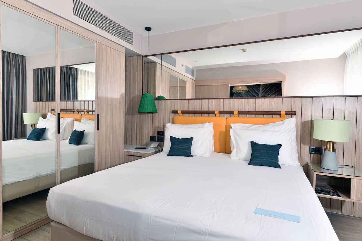 A modern hotel room with a large bed, a mirror, a bedside table, and a nightstand.