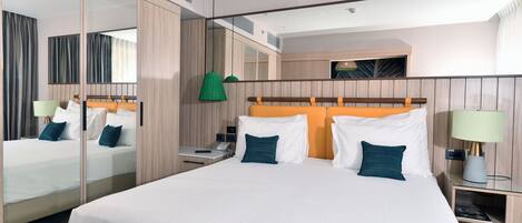 A modern hotel room with a large bed, a mirror, a bedside table, and a nightstand.