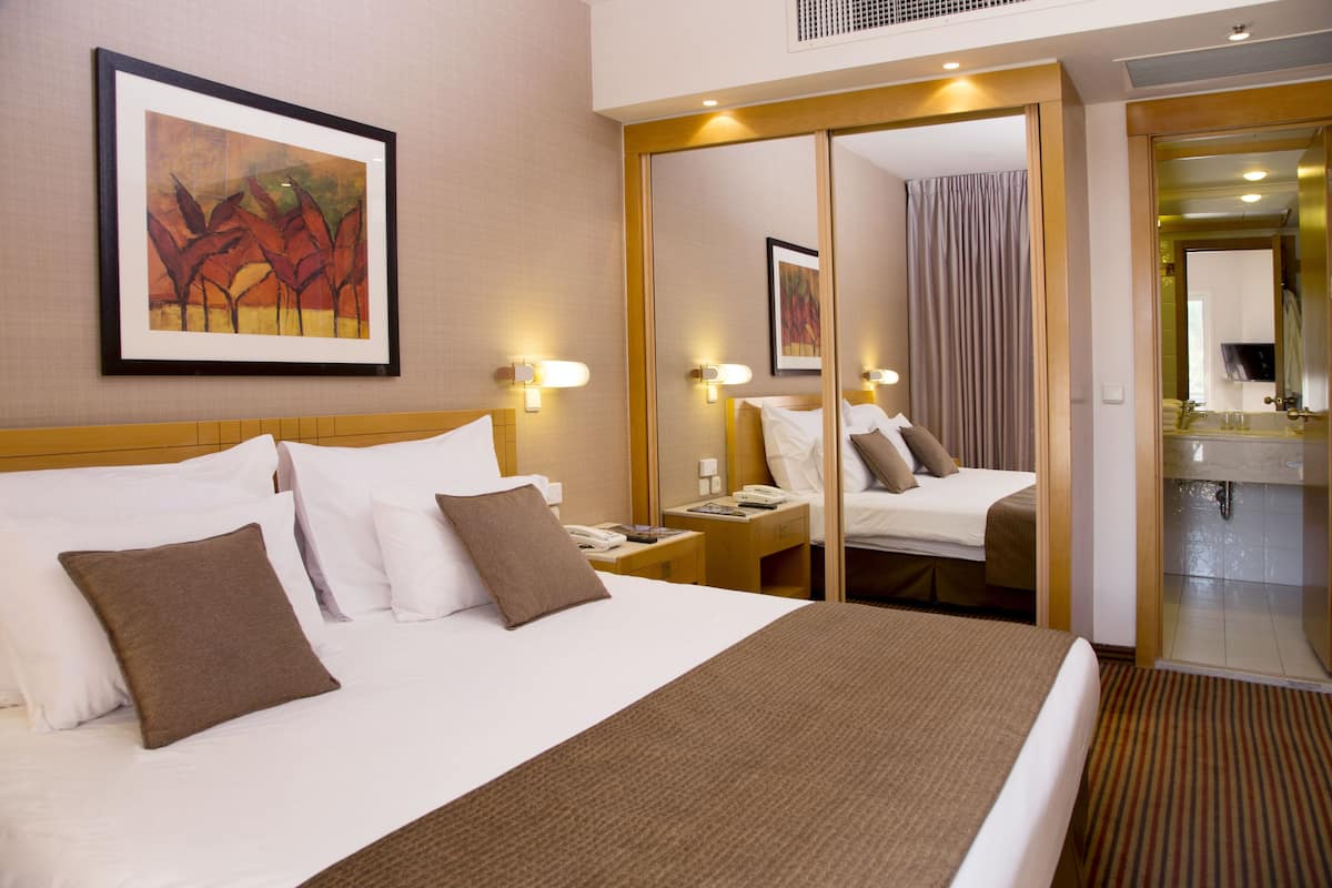 A hotel room with a large bed, a nightstand, a mirror, and a bathroom visible through an open door.