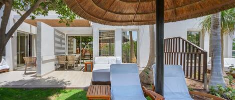 A modern outdoor lounge area with two lounge chairs, a wooden table, and a thatched umbrella.