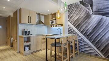 A modern kitchen with wooden cabinets, a microwave, and a coffee machine. There are two bar stools and a large leaf-patterned wall mural.