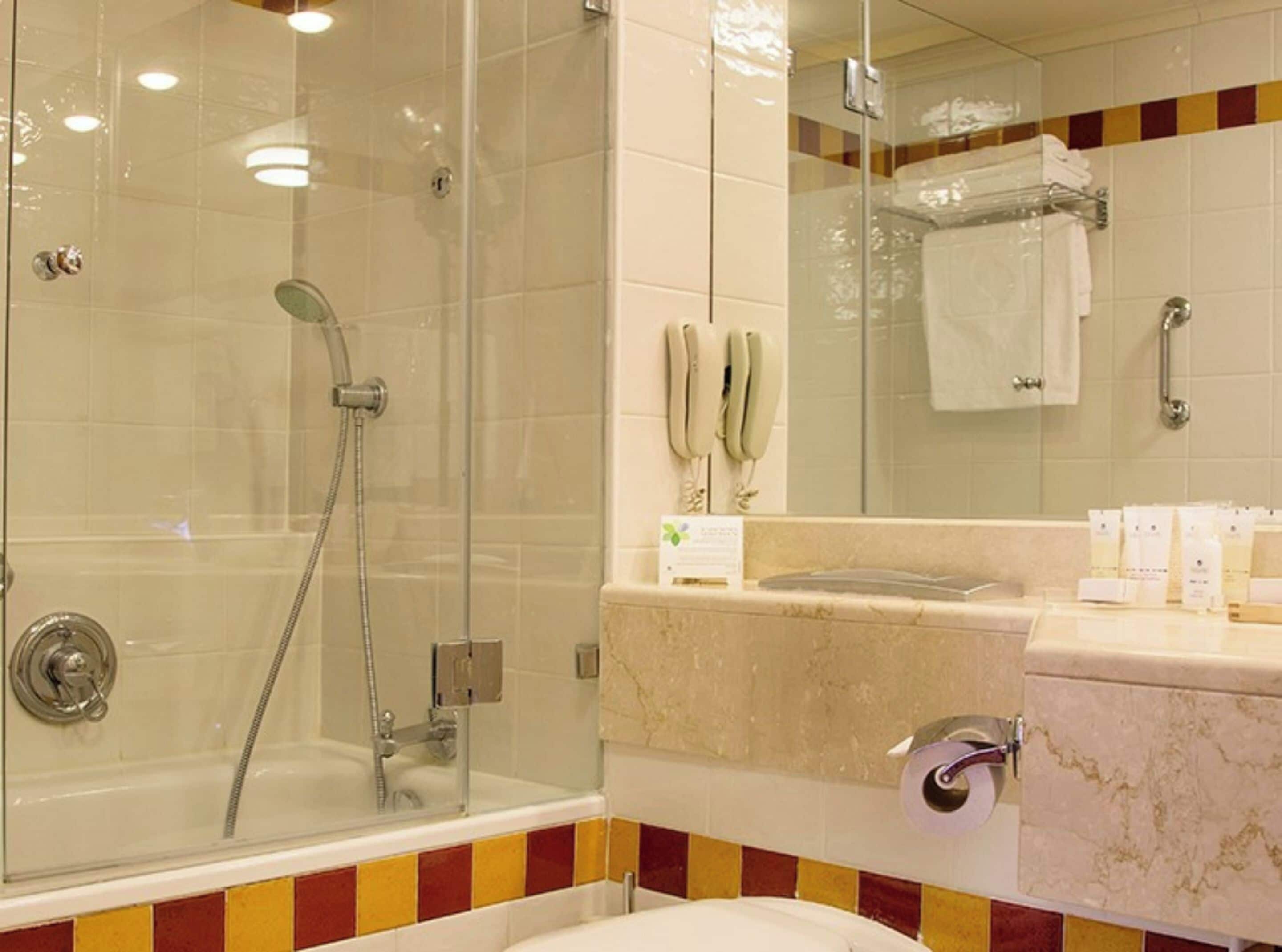Un baño moderno con ducha envuelta en vidrio, tocador de mármol y espejo sobre el lavabo.