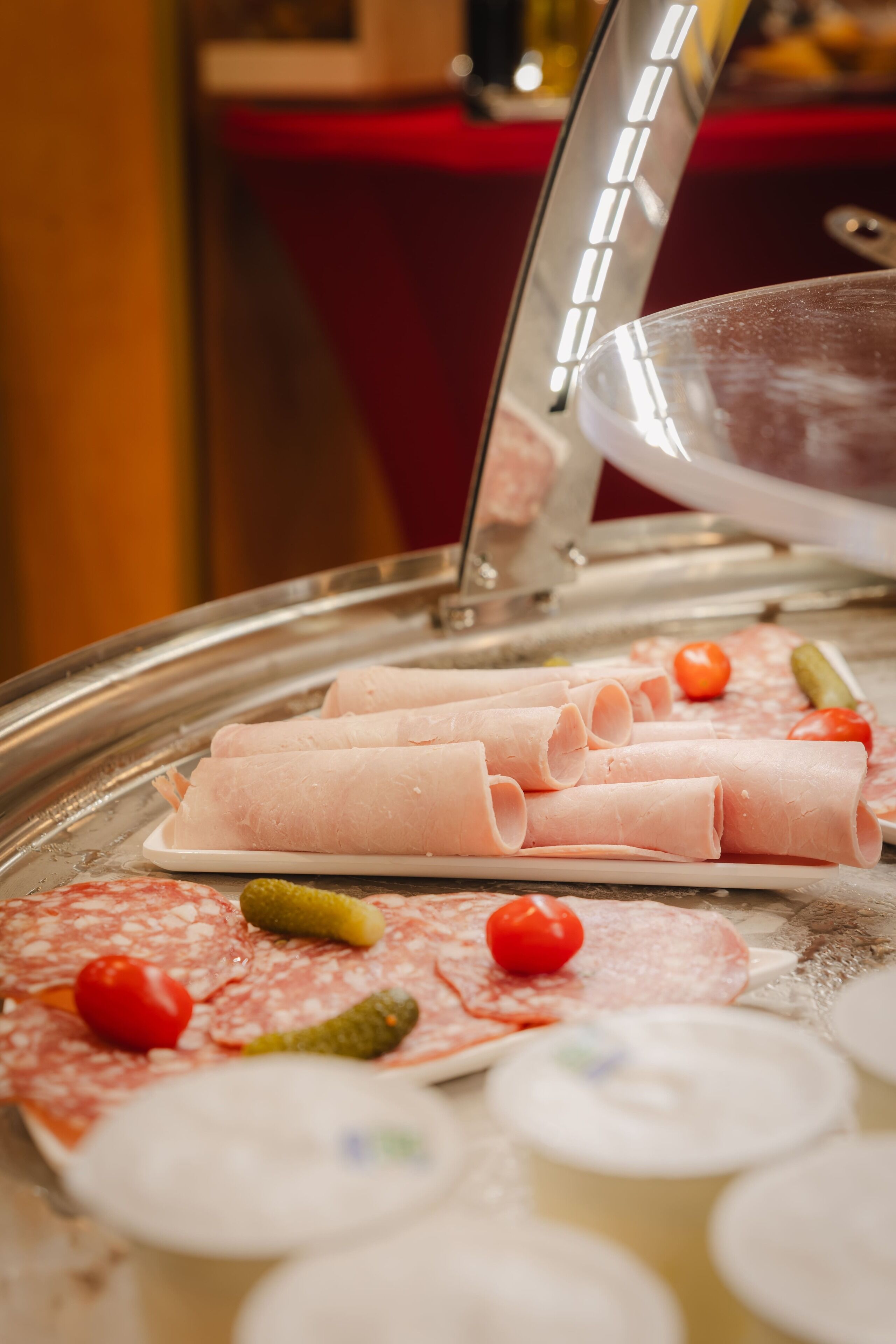 A buffet with various cold cuts, pickles, and tomatoes.