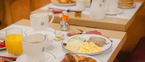 A breakfast table with plates of eggs, croissants, and juice.