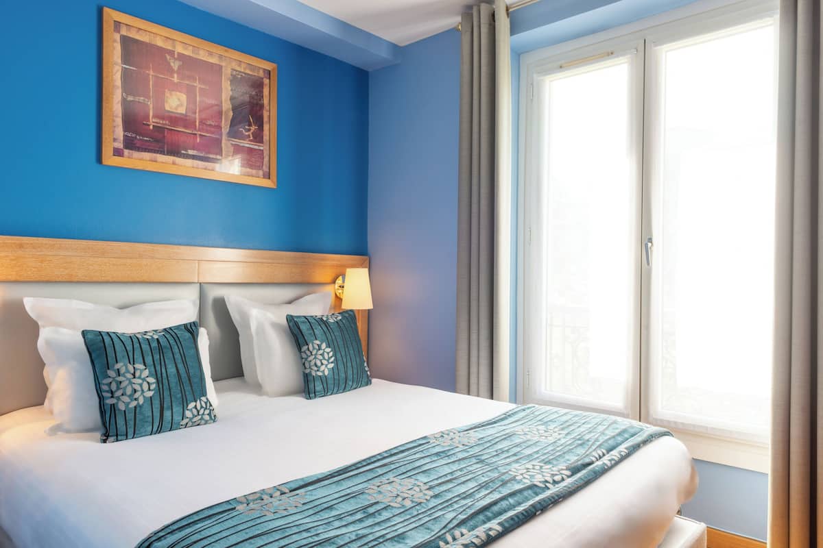 Habitación de hotel con una cama grande, cabecero, ventana con cortinas e imagen enmarcadas en la pared.