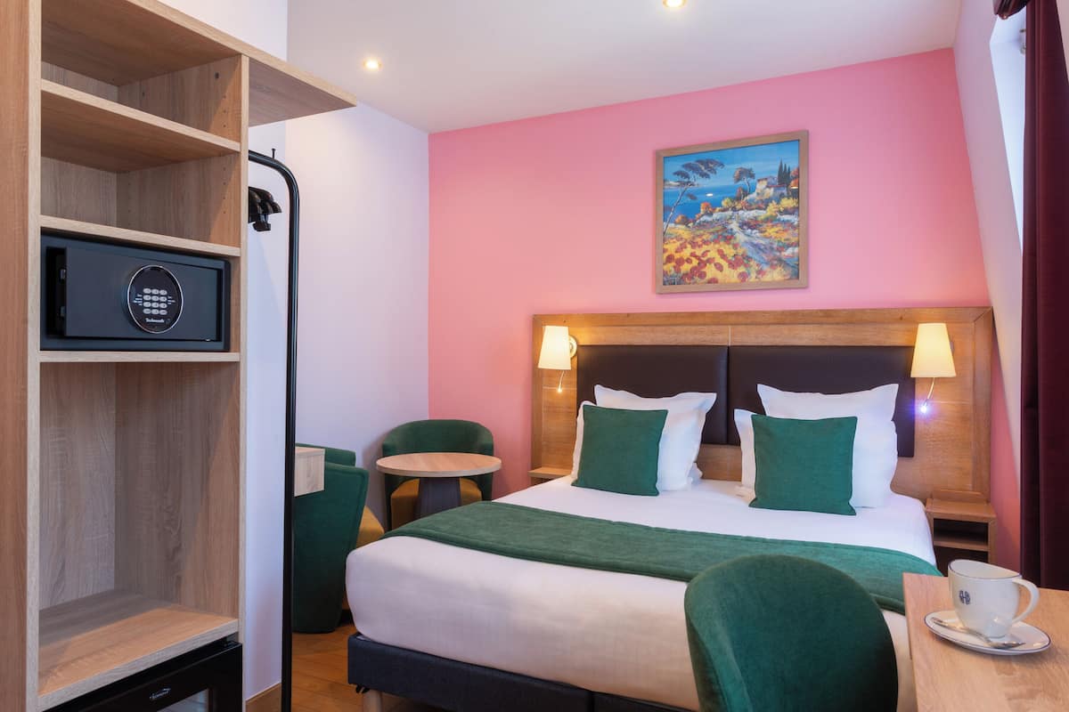 Una habitación de hotel con una cama, un cuadro en la pared, un escritorio con una taza y una silla verde.
