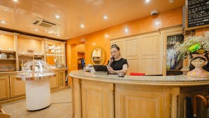 A reception area with a counter, a woman at the counter, and a decorative mirror on the wall. - Grand Hotel Dore (Paris)