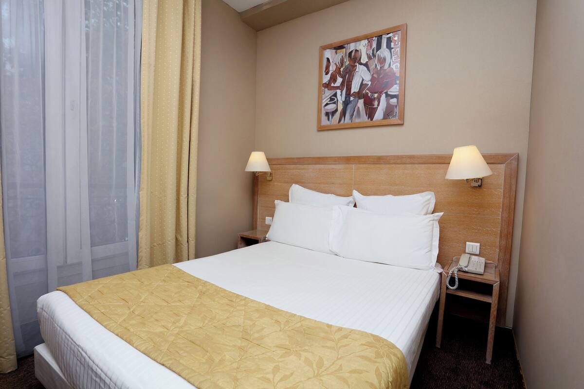 Een hotelkamer met een bed, twee bedlampen, een nachtkastje met een telefoon en een schilderij aan de muur.
