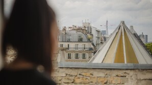 A person holding a piece of paper near a stone wall with a view of buildings in the background. - Grand Hotel Dore (Paris)