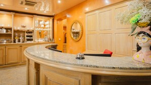 A kitchen with a curved granite countertop, wooden cabinets, and a decorative ceramic figure. - Grand Hotel Dore (Paris)