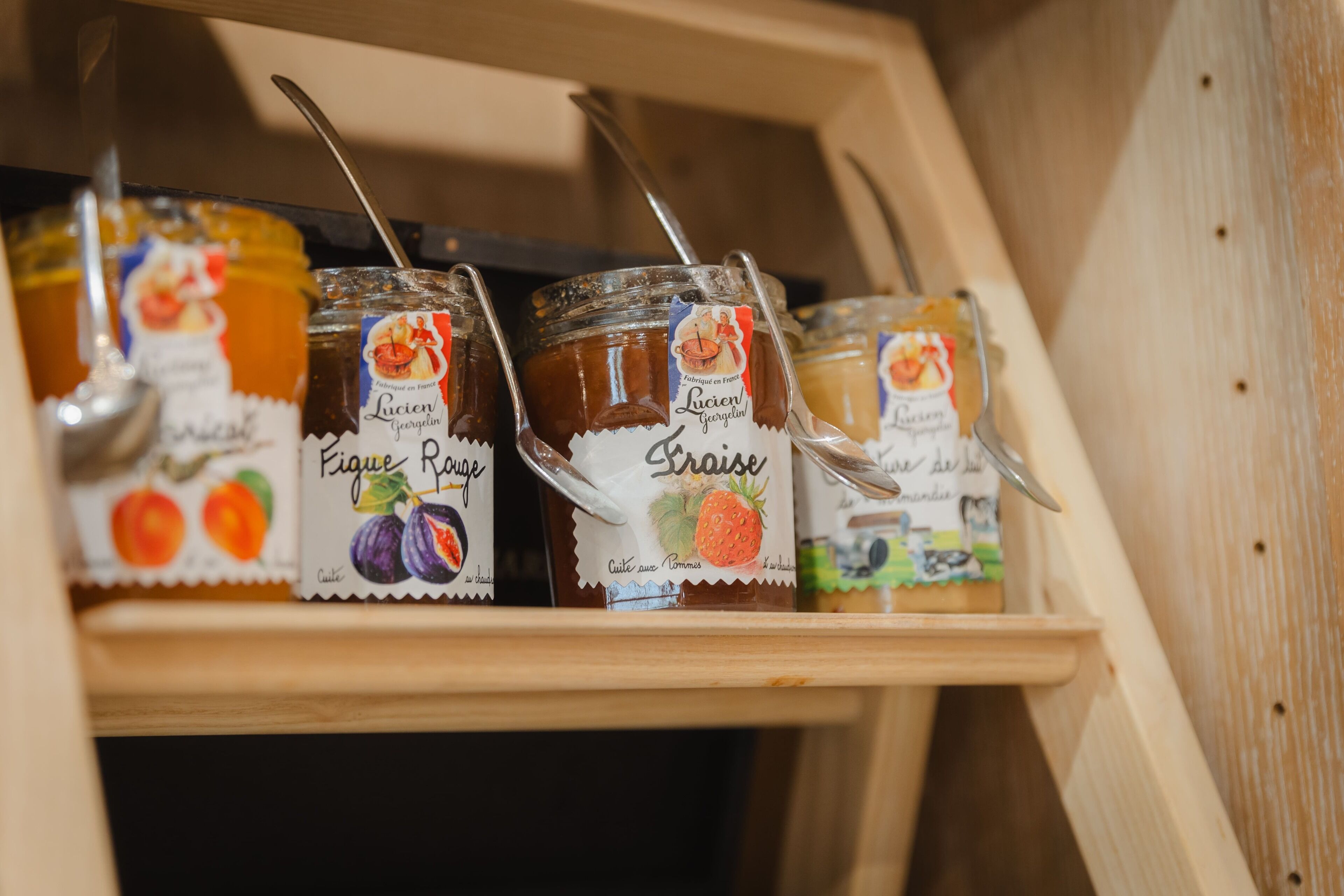 A wooden shelf with jars of Lucien Georgesin fig and strawberry preserves.