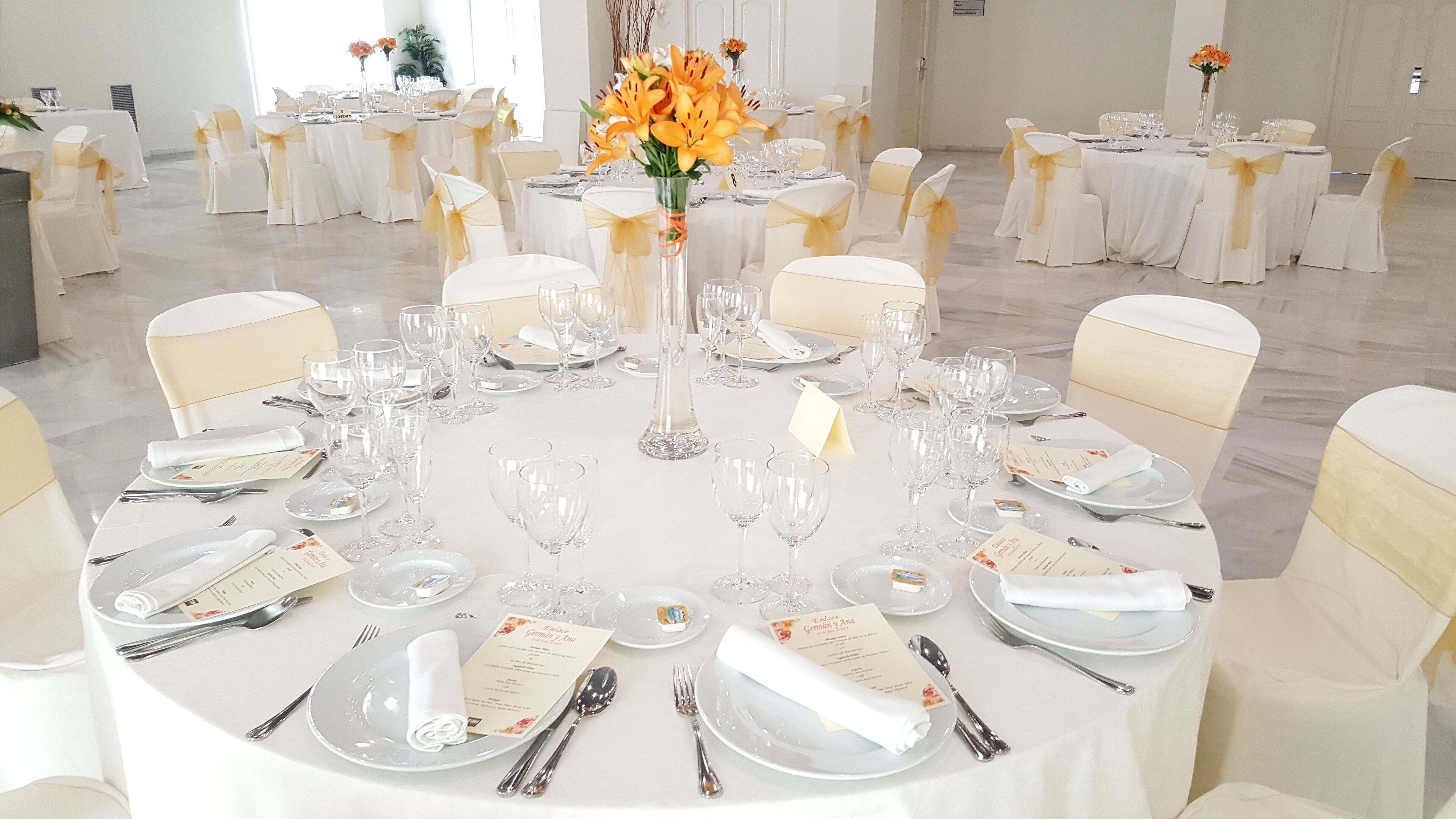 Une table ronde dressée pour un événement officiel, avec des nappes blanches, des rubans dorés et de la verrerie transparente.