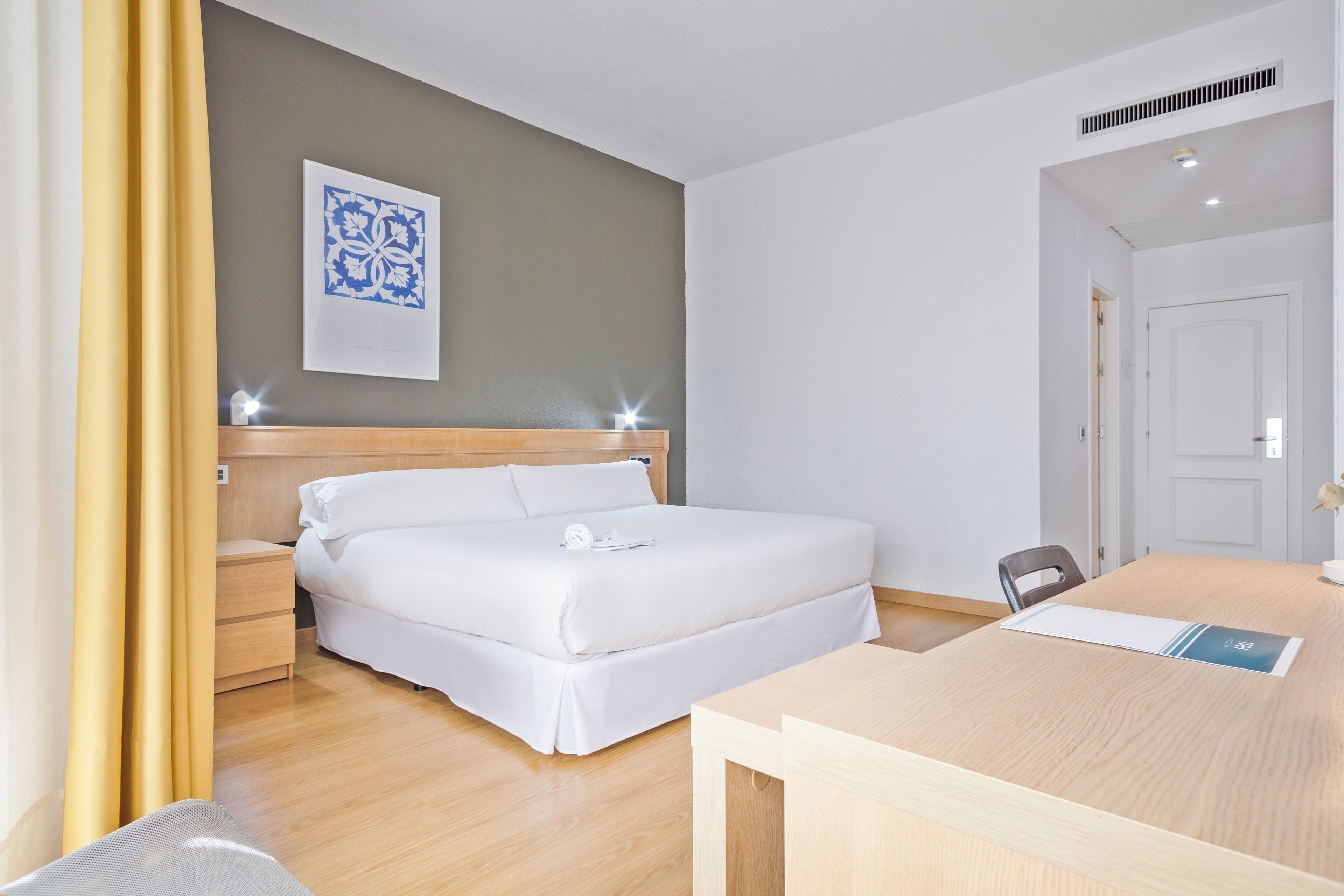 A hotel room with a bed, bedside tables, a desk, and a chair.