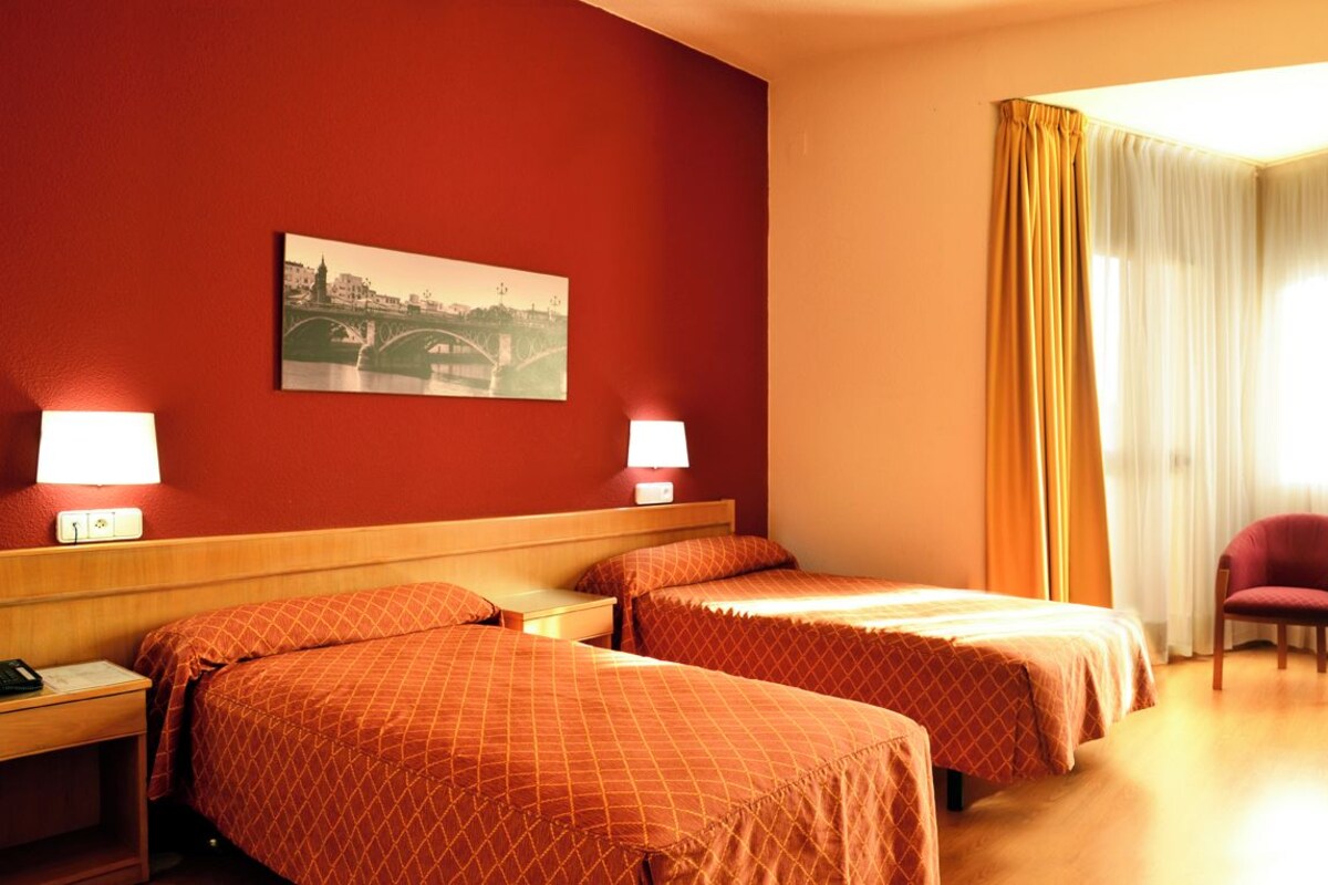 A hotel room with two beds, a desk, a chair, and a painting on the wall.