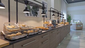 A breakfast buffet with various baked goods and pastries, a coffee machine, and a seating area with a plant.