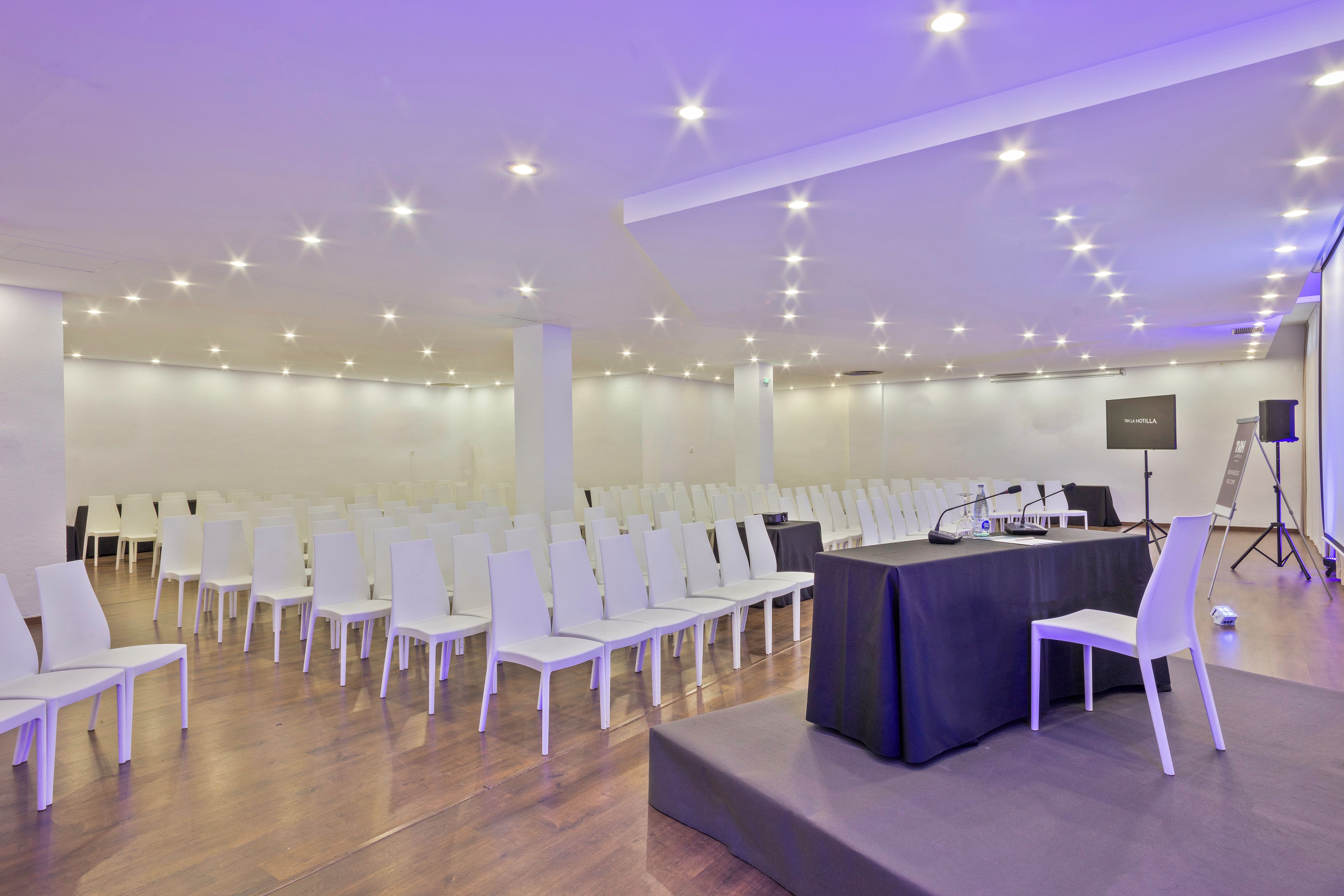 A conference room with rows of white chairs, a stage with a table, and a podium.