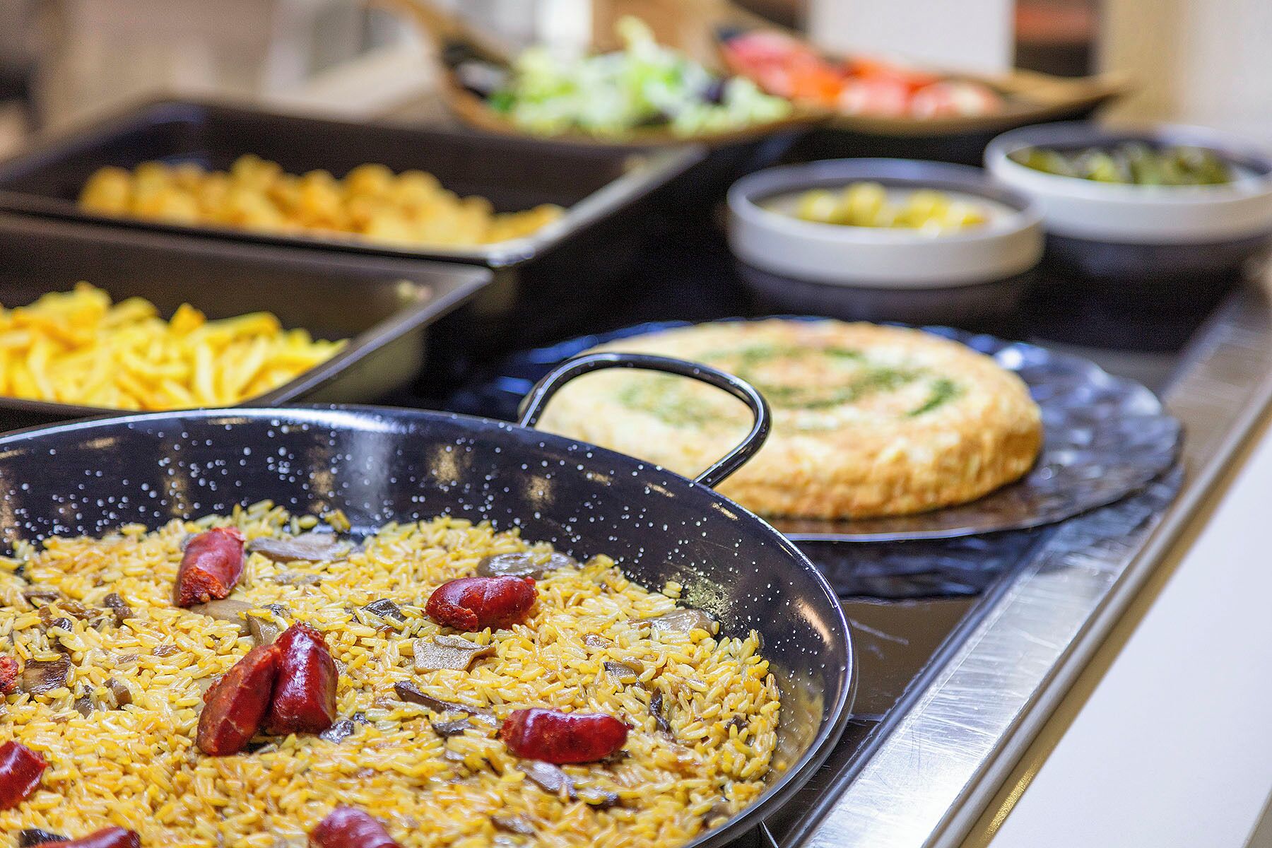Een buffet met diverse gerechten, waaronder rijst, worstjes en een groentegerecht.