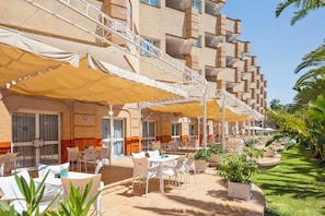 An outdoor seating area with tables and chairs, a covered walkway, and a building with multiple balconies. - Hotel TRH La Motilla (Dos Hermanas)