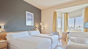 A hotel room with two beds, a desk, a chair, a TV, and a window with curtains.