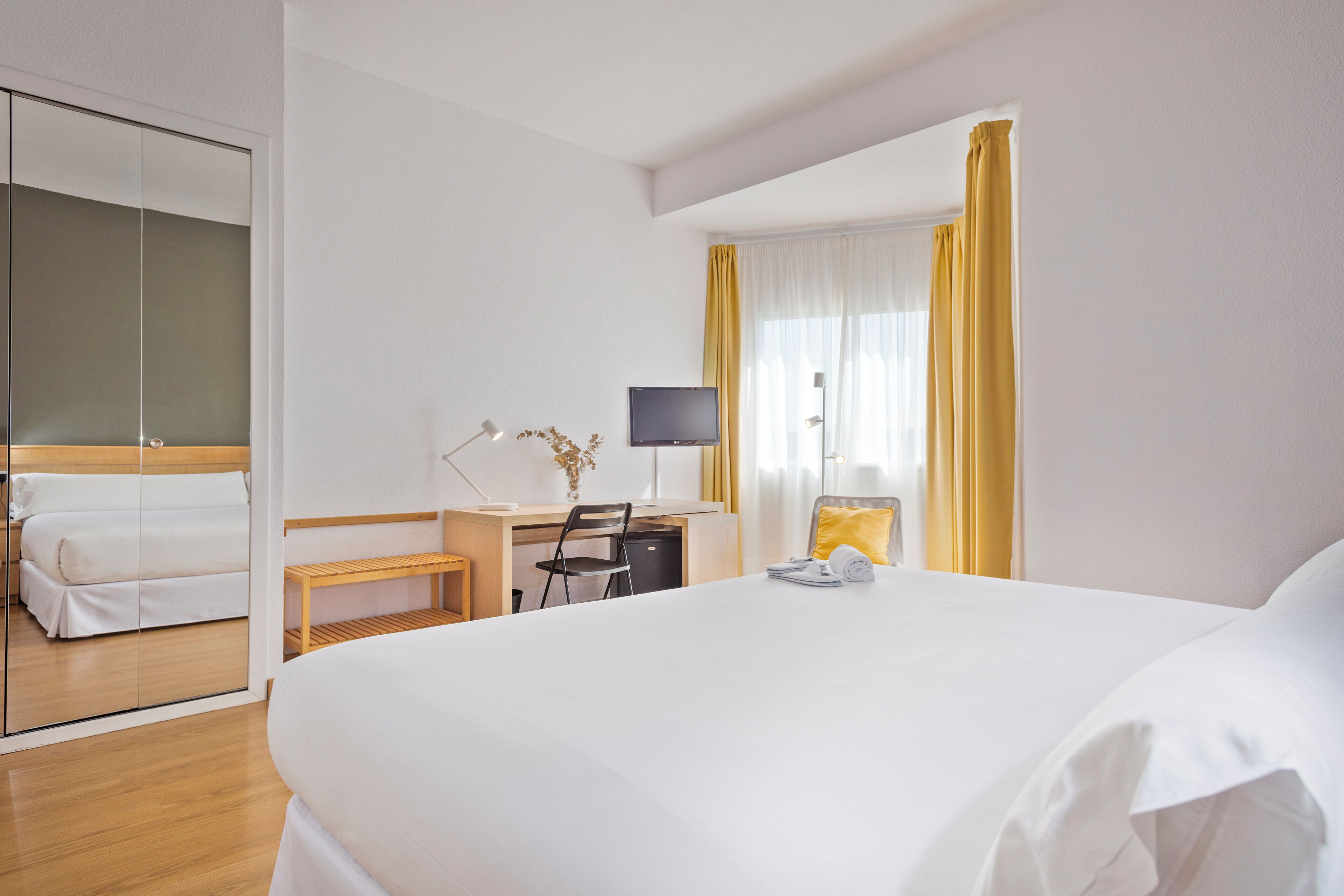 A hotel room with a bed, a desk with a computer, a chair, and a TV.