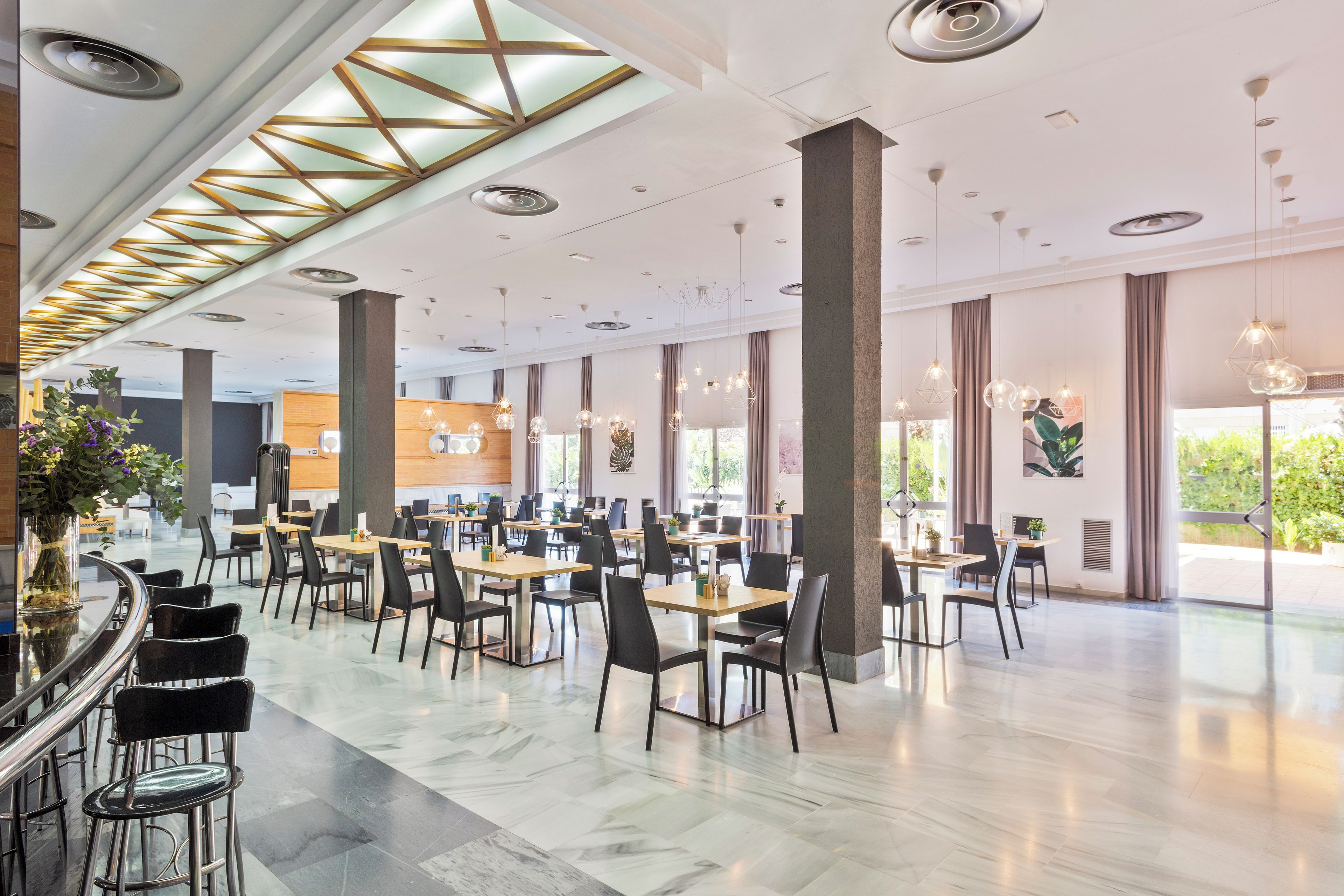 Un vaste espace de restauration intérieur, doté de nombreuses tables et chaises, de grandes fenêtres et d’un design de plafond moderne.