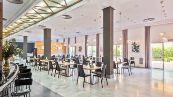 Un vaste espace de restauration intérieur, doté de nombreuses tables et chaises, de grandes fenêtres et d’un design de plafond moderne.