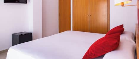 A hotel room with a bed, a TV mounted on the wall, a wardrobe, and a bedside lamp.