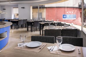 A restaurant with tables set for dining, a blue counter, and a view of the outside.