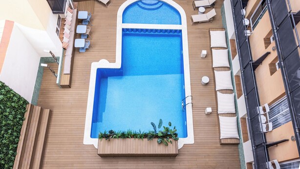 A rooftop pool with a wooden deck, lounge chairs, and a planter with plants. - RVHotels Mar de Tossa (Tossa de Mar)