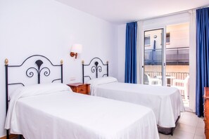 A hotel room with two beds, a nightstand, a lamp, and a balcony with blue curtains.