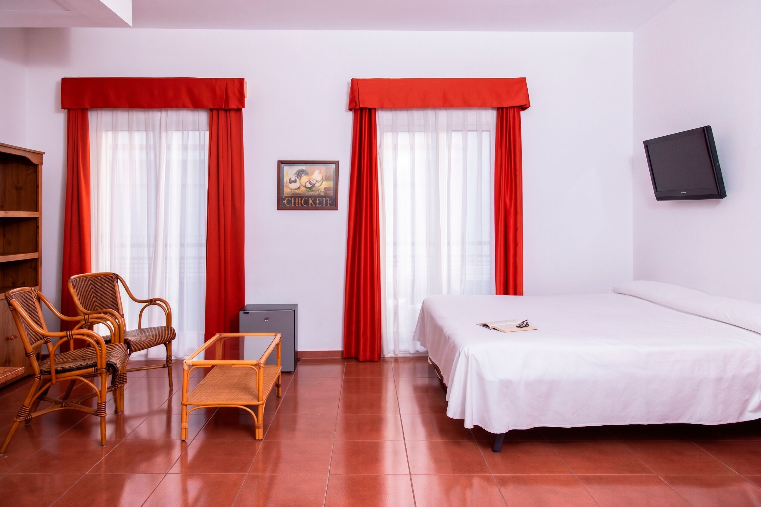 A room with a bed, two chairs, a small table, a TV, and a picture on the wall.