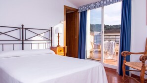 A hotel room with a bed, a nightstand, a lamp, a chair, and a view of the outside. - RVHotels Mar de Tossa (Tossa de Mar)