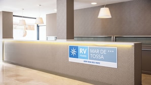 A reception desk with a sign for RV Mar de Tossa, a modern interior with a marble floor, pendant lighting, and a textured wall. - RVHotels Mar de Tossa (Tossa de Mar)