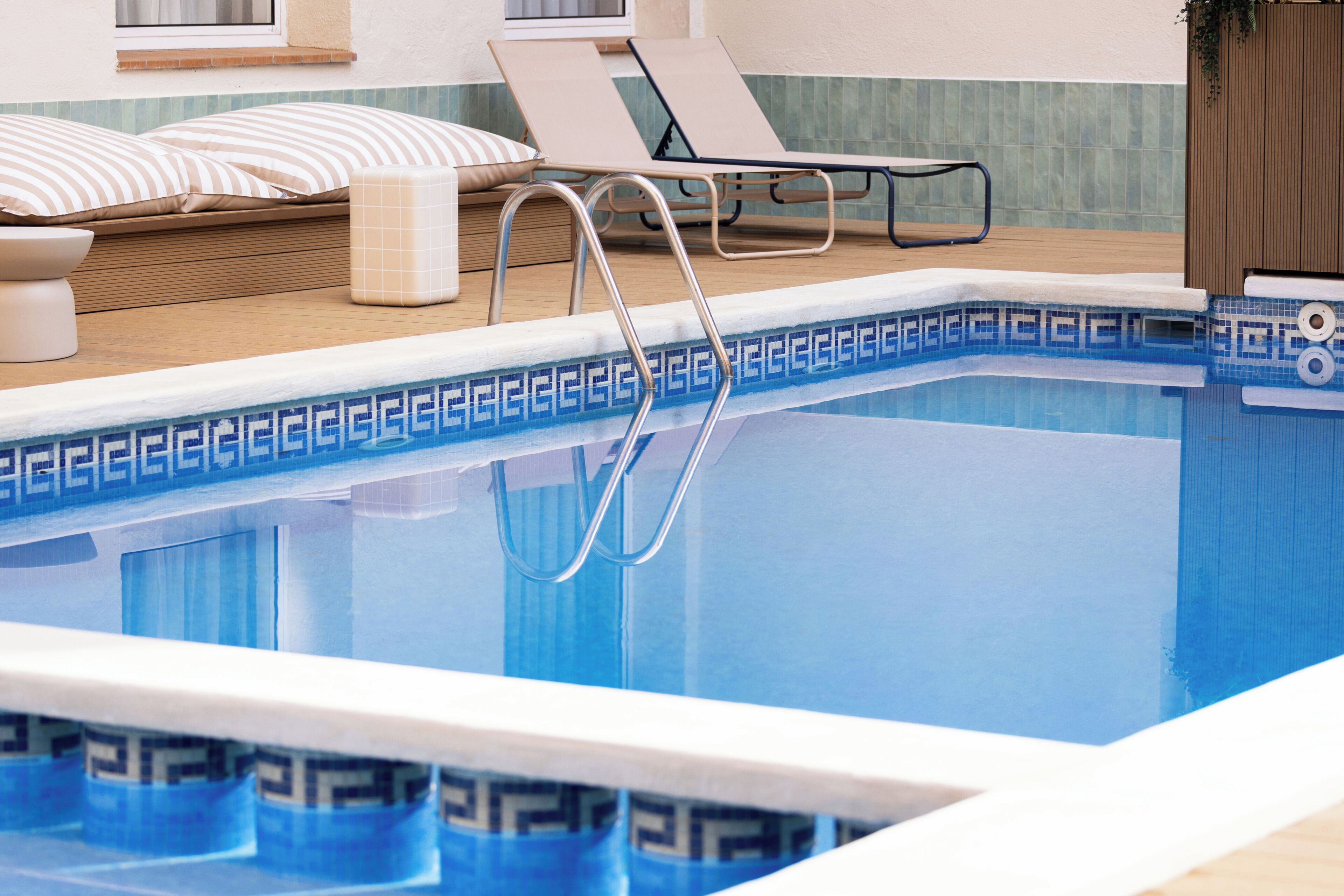 A swimming pool with a tiled edge, a wooden deck, and lounge chairs.