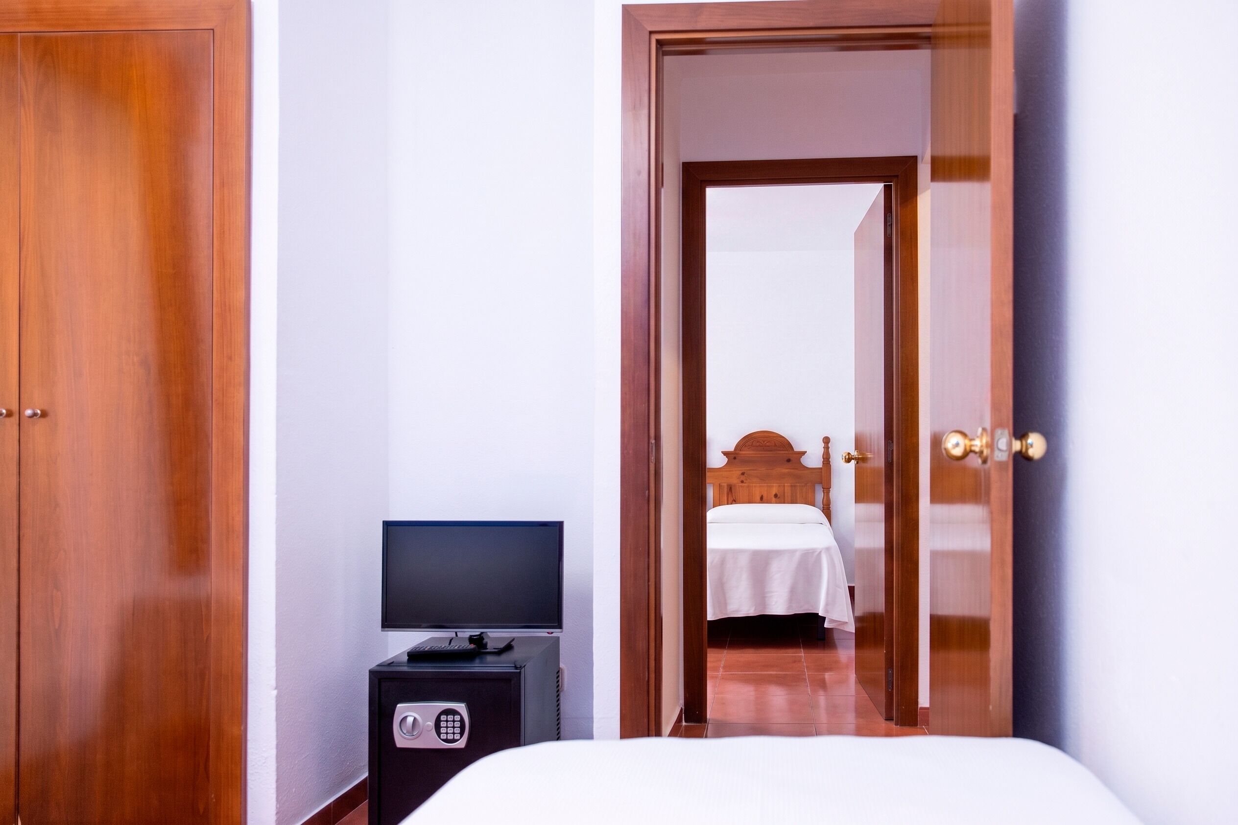 A hotel room with a wooden wardrobe, a television on a small cabinet, and a bed with a wooden headboard.
