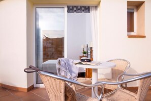 A balcony with wicker chairs, a small round table, and a view of a building through a glass door.