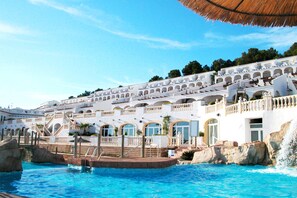 Um resort com uma piscina grande, edifícios brancos com varandas e um céu azul límpido.