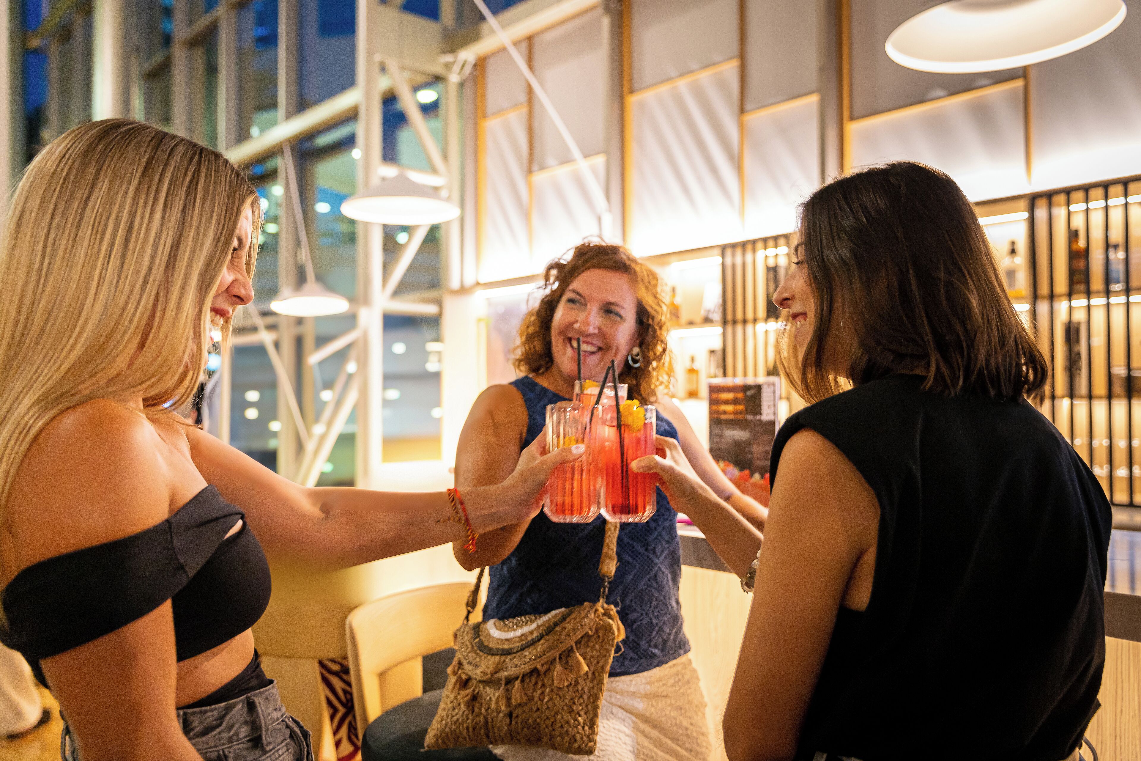 Tres personas brindando con bebidas en un ambiente interior moderno con amplios ventanales y mobiliario contemporáneo.
