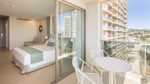 A hotel room with a bed, a balcony with a table and chairs, and a view of other buildings. - AR Diamante Beach Spa & Convention Center (Calpe)