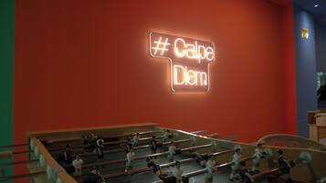 Un letrero de neón con el hashtag #CalpeDiem, una mesa de fútbol de mesa y una pared roja.