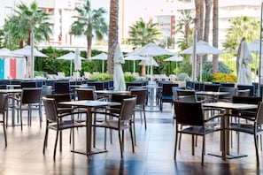 An outdoor dining area with tables and chairs, umbrellas, and palm trees. - AR Diamante Beach Spa & Convention Center (Calpe)