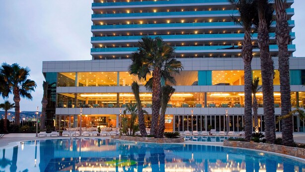 A hotel with a pool, palm trees, and a modern building with illuminated windows. - AR Diamante Beach Spa & Convention Center (Calpe)