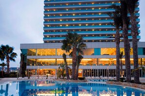 A hotel with a pool, palm trees, and a modern building with illuminated windows. - AR Diamante Beach Spa & Convention Center (Calpe)