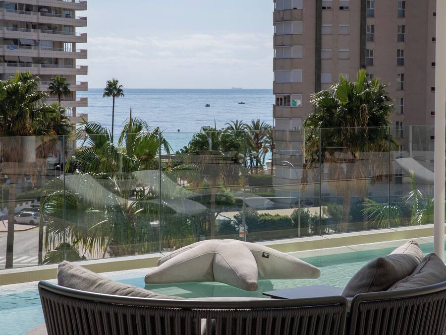 Een loungehoek bij het zwembad met uitzicht op de oceaan en palmbomen.