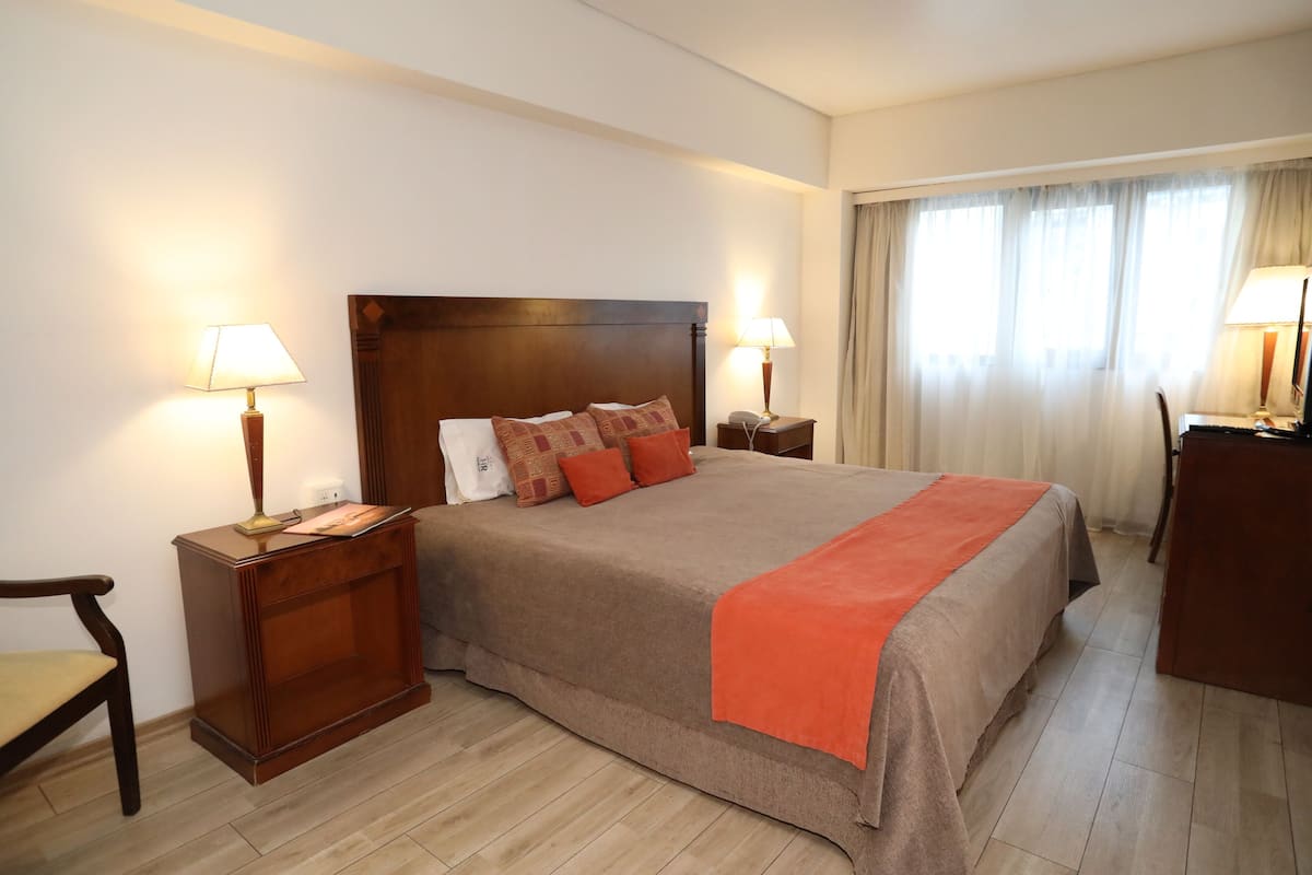 A hotel room with a large bed, two bedside tables with lamps, a wooden chair, and a desk.