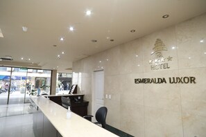 A hotel reception area with a marble wall, a reception desk, and a door. - HR Esmeralda Luxor (Buenos Aires)