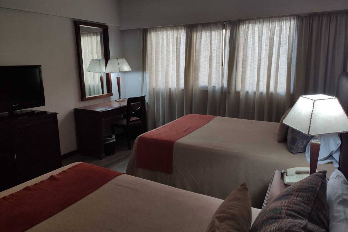 A hotel room with two beds, a desk, a chair, a television, and a lamp.