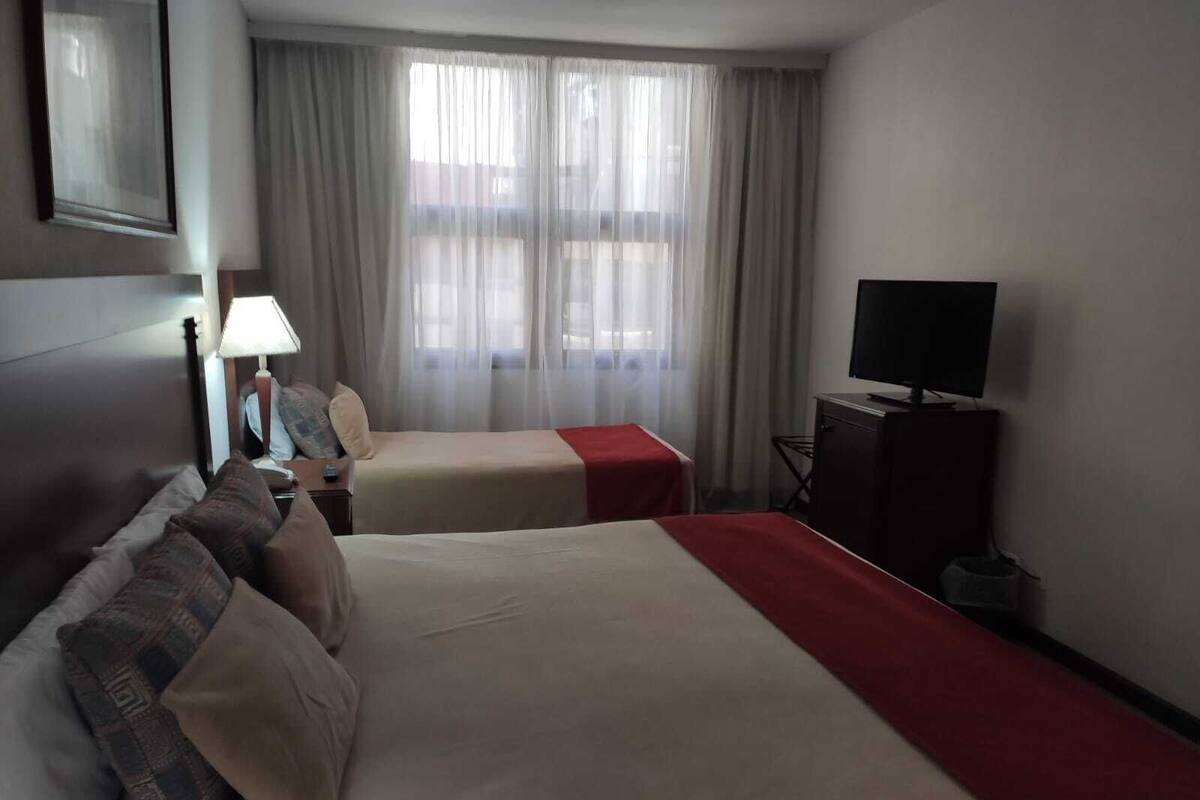 A hotel room with two beds, a TV, a desk, and a lamp.