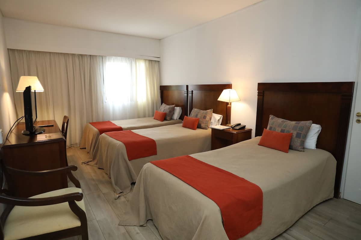 A hotel room with two beds, a desk, a chair, and a lamp.